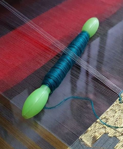 A green bobbin of silk thread on the loom